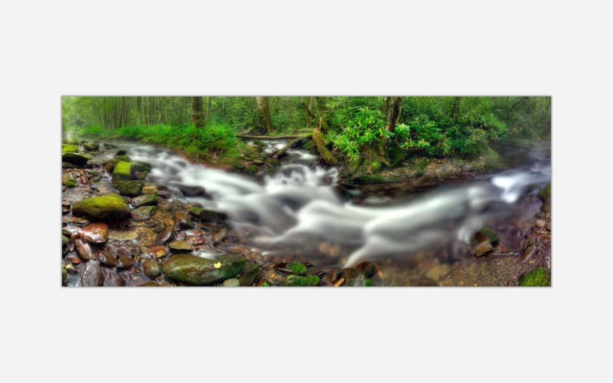 Long exposure photograph of a serene river flowing through a misty forest with moss-covered rocks.