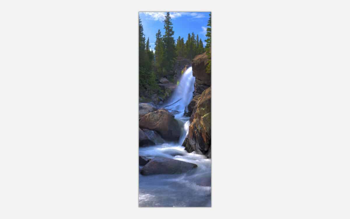 A vertical panoramic photograph of a beautiful cascading waterfall surrounded by forest and rocks, ideal for wall decor.