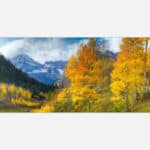 A panoramic landscape photo art of a mountain range with layers of yellow aspen trees in fall color in the foreground.