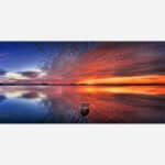 A panoramic painting of a tranquil lake sunset with vibrant sky colors reflected in the water and a lone boat.