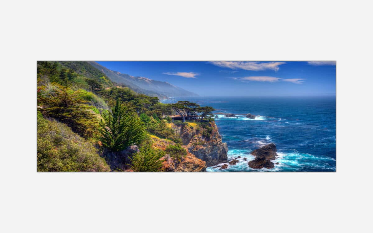 A panoramic view of a coastal landscape with a rocky shoreline, blue ocean, greenery, and a clear sky.