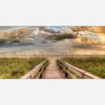A panoramic art print of a serene beach scene with a wooden path leading to the ocean, featuring lush beach grass, a cloudy sky, and a warm sunset glow.