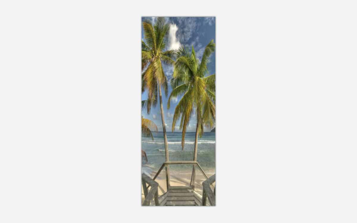 A vertical panoramic art print of a wooden staircase leading down to a serene beach flanked by tall palm trees with a beautiful blue ocean in the background.