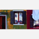 A photograph capturing a colorful urban scene with a green and orange textured wall, a red door, and two windows, one adorned with flowers and the other with hanging laundry.