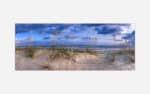 Panoramic image of a serene beach landscape with sand dunes and beach grass under a blue sky with clouds.