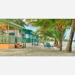 A vibrant painting of colorful beachfront cabins with palm trees on a sandy tropical beach.