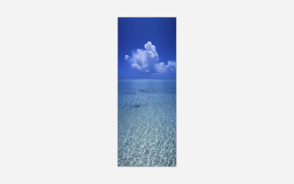 A vertical panoramic image of clear blue ocean water with a detailed cloud formation in the sky above