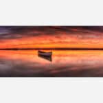 A photographic art piece featuring a serene lake with a solitary boat, vibrant sunset skies with clouds reflected in the calm waters.