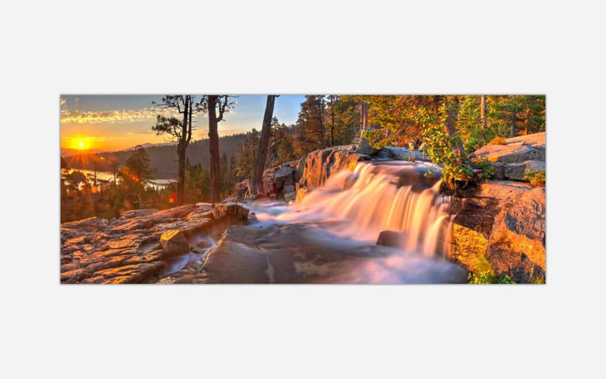 An artful photograph of a waterfall with the sun rising in the background, illuminating the trees and water with a warm golden light, suitable for decorative wall art.