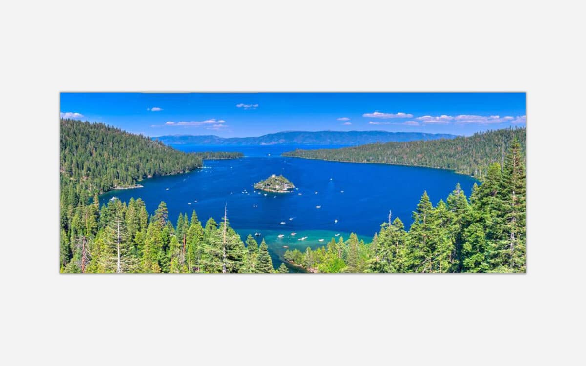 Panoramic view of the blue waters of Lake Tahoe with surrounding green forests and mountain ranges under a clear sky.