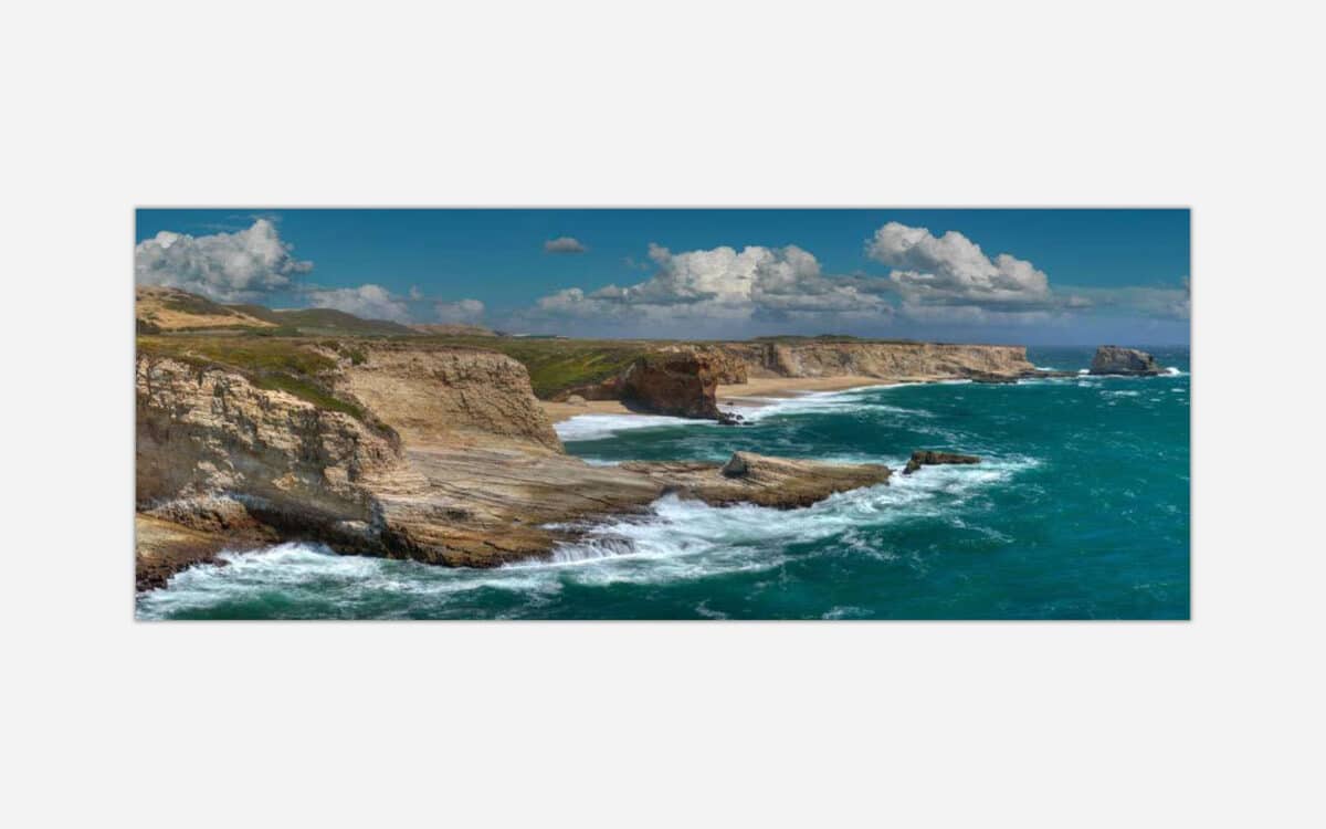 A seascape wall art depicting turquoise ocean waters crashing against rugged cliffs under a cloudy blue sky.