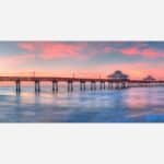 A serene image of a long pier extending into calm waters under a pastel-colored sunset sky.