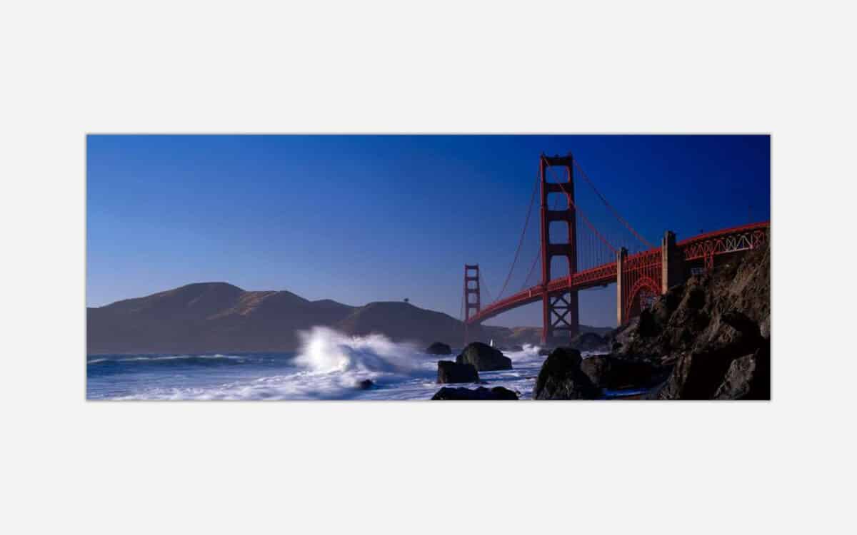 Golden Gate Bridge with ocean waves crashing on the shore and a clear blue sky in the background.