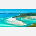Aerial photograph of a scenic tropical beach with turquoise waters and white sand surrounded by lush greenery.