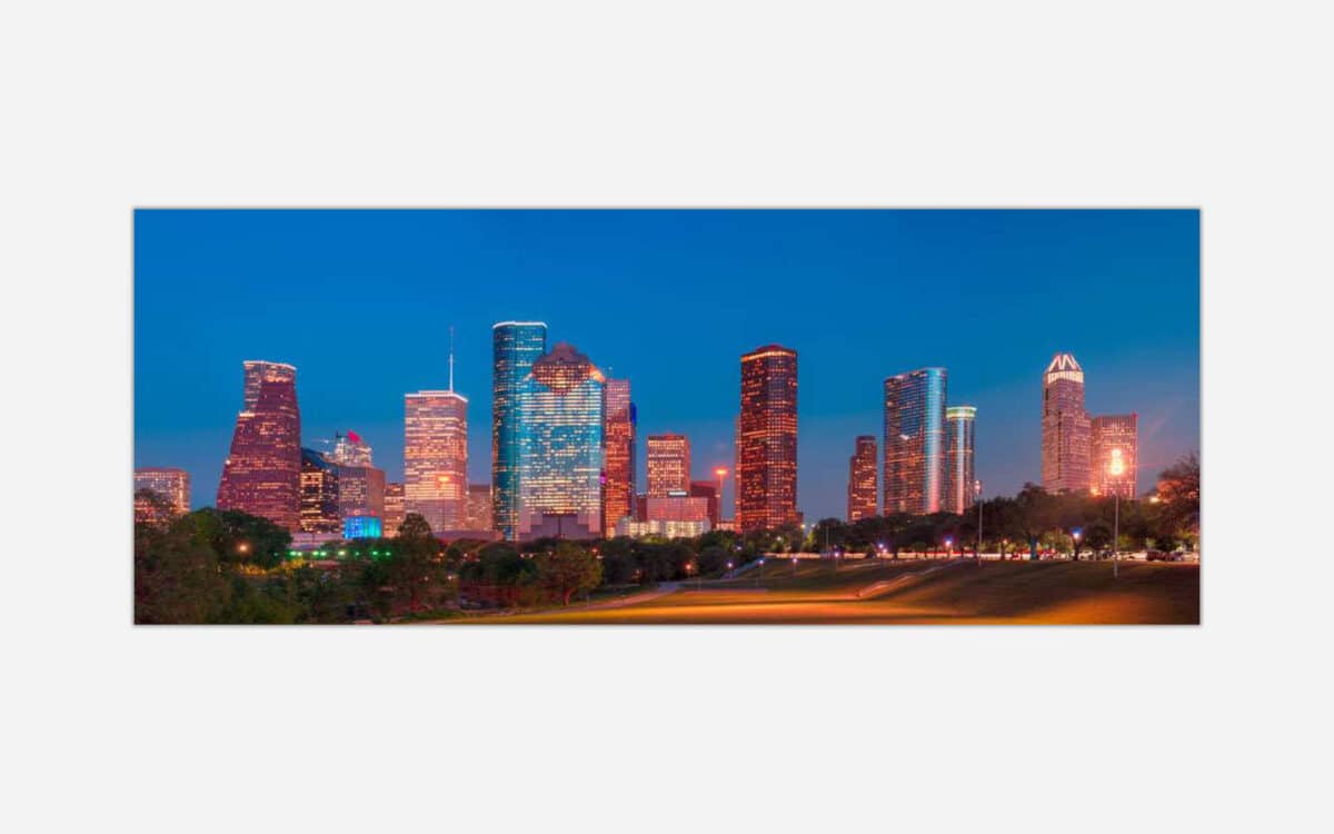 An image of the Houston city skyline at dusk with illuminated buildings and a clear sky.