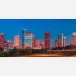 An image of the Houston city skyline at dusk with illuminated buildings and a clear sky.