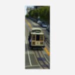 A tilt-shift photograph of a classic San Francisco cable car on the streets with blurred surrounding details giving a miniature effect.