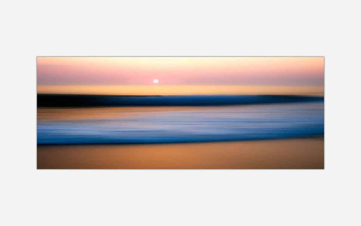 A blurred image of a beach scene at sunset with pastel colors and a tranquil ocean, creating an abstract seascape suitable for modern wall decor.