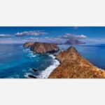 A panoramic photograph of a rocky coastal landscape with blue seas, distant islands, and a clear sky.