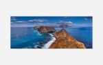 A panoramic photograph of a rocky coastal landscape with blue seas, distant islands, and a clear sky.