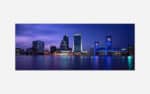 A panoramic view of a city skyline at twilight with illuminated high-rise buildings and a distinctive blue bridge reflected on the water's surface.