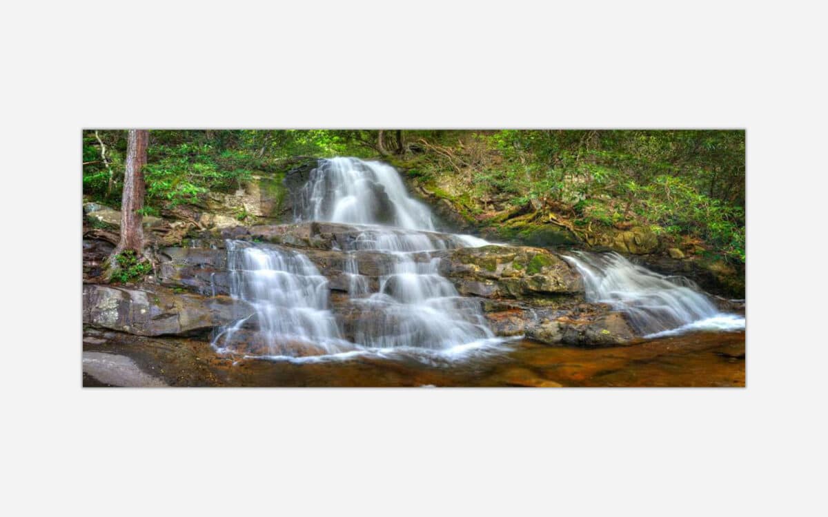 A photograph of a small, serene waterfall with silky smooth water cascading over rocks in a lush forest setting.