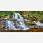 A photograph of a small, serene waterfall with silky smooth water cascading over rocks in a lush forest setting.