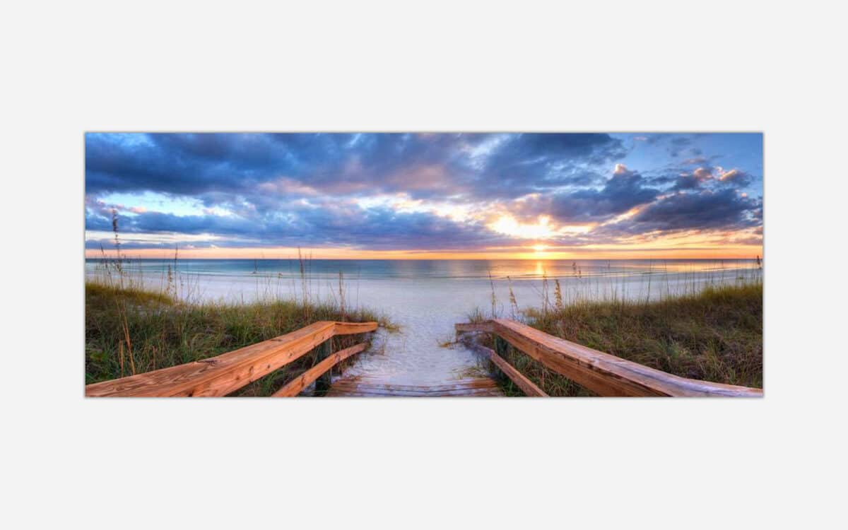 A canvas print of a tranquil beach scene at sunset with a wooden pathway leading through dunes to the shore, with vibrant colors in the sky and reflections on the water.