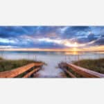 A canvas print of a tranquil beach scene at sunset with a wooden pathway leading through dunes to the shore, with vibrant colors in the sky and reflections on the water.