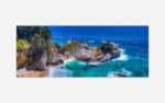 Aerial view of a vibrant coastal landscape featuring a turquoise ocean, white sandy beach, rocky cliffs, and a waterfall amidst lush greenery.