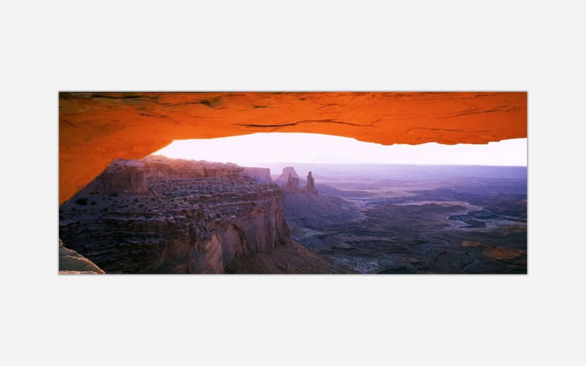 A photo of Mesa Arch in Canyonlands National Park capturing the warm glow of sunrise over the rugged canyons and rock formations.