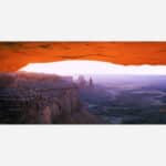 A photo of Mesa Arch in Canyonlands National Park capturing the warm glow of sunrise over the rugged canyons and rock formations.