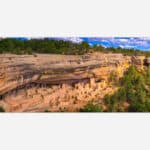 A panoramic photograph of the ancient cliff dwellings at Mesa Verde National Park, showcasing the intricate structures and surrounding natural environment.