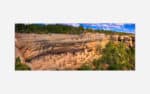 A panoramic photograph of the ancient cliff dwellings at Mesa Verde National Park, showcasing the intricate structures and surrounding natural environment.