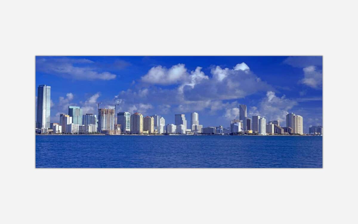 Alt text: An expansive view of a modern city skyline with numerous high-rise buildings along the oceanfront under a blue sky with fluffy clouds.