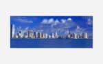 Alt text: An expansive view of a modern city skyline with numerous high-rise buildings along the oceanfront under a blue sky with fluffy clouds.