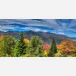 A panoramic photograph of a mountain range with colorful autumn foliage and a predominantly blue sky with scattered clouds.