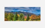 A panoramic photograph of a mountain range with colorful autumn foliage and a predominantly blue sky with scattered clouds.