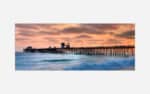 A serene sunset over a wooden ocean pier with vibrant sky colors and a calm sea.