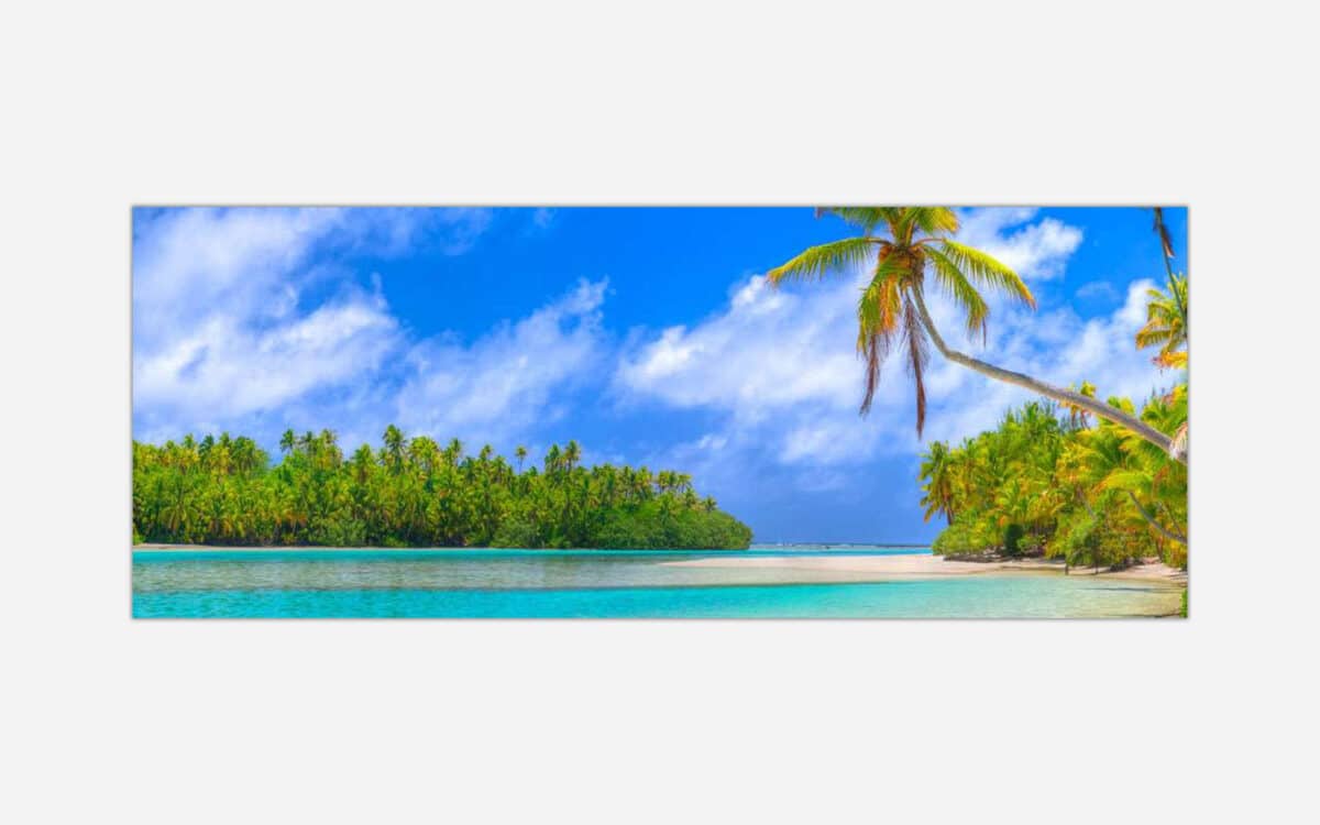A panoramic view of a tropical beach with clear turquoise water, palm trees, and a blue sky with white clouds.