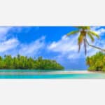 A panoramic view of a tropical beach with clear turquoise water, palm trees, and a blue sky with white clouds.