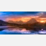 A serene mountain landscape at sunset with vibrant colors in the sky reflecting on a calm lake.