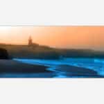 A painting of a sunset view at a coastal scene with a lighthouse overlooking a beach with crashing blue waves.