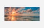 A scenic view of a beach at sunset with a vibrant sky reflected on the ocean and wet sand.