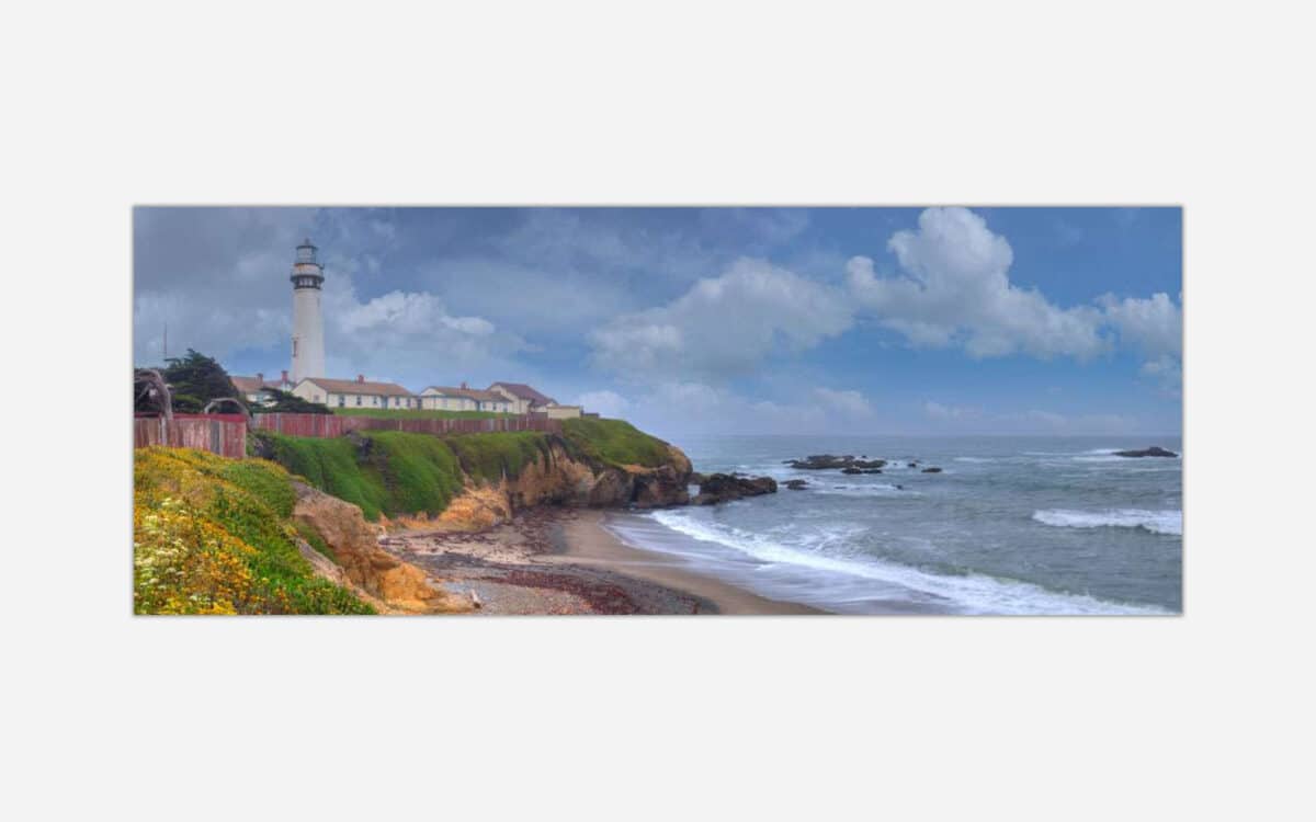 A painting of a lighthouse on a cliff overlooking a beach with waves and cloudy skies.