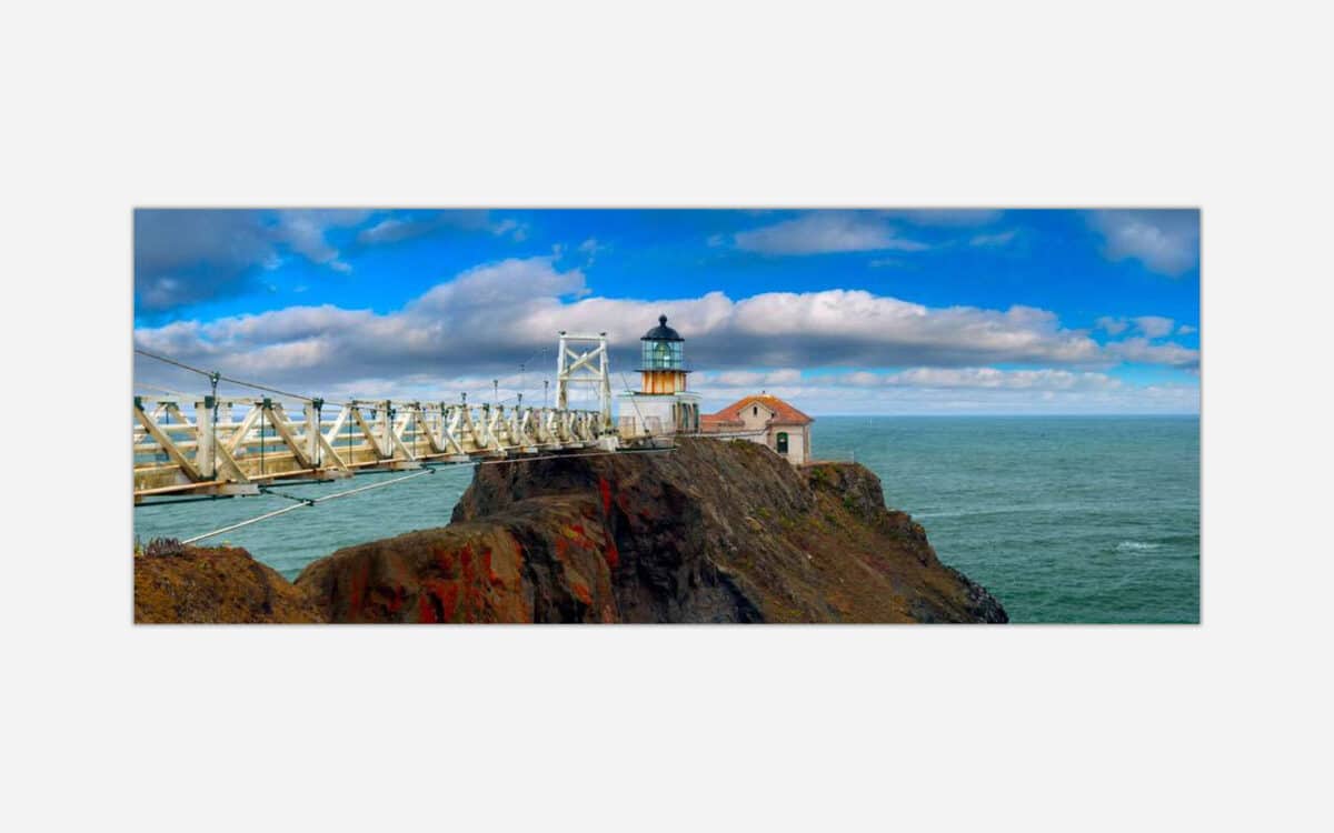 A panoramic art piece depicting a historic lighthouse on a rocky coastline with a footbridge leading up to it under a dynamic sky with scattered clouds.