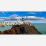 A panoramic art piece depicting a historic lighthouse on a rocky coastline with a footbridge leading up to it under a dynamic sky with scattered clouds.