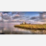 A scenic artwork depicting a white lighthouse on a grassy coastal area with a serene waterfront and a sky filled with clouds at sunset.