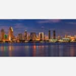 A panoramic view of a city skyline at twilight with illuminated buildings reflecting on the water.