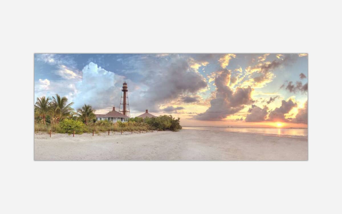 Panoramic view of a tranquil beach scene at sunset with a lighthouse and lush greenery.